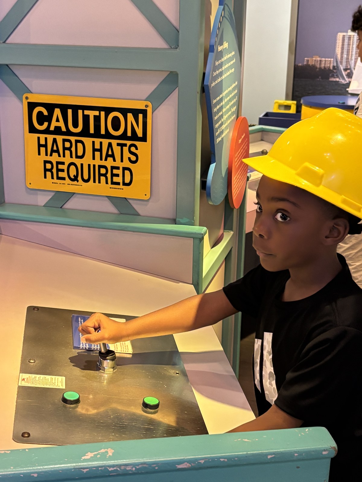 Child in yellow hard hat at an engineering exhibit during a STEM field trip